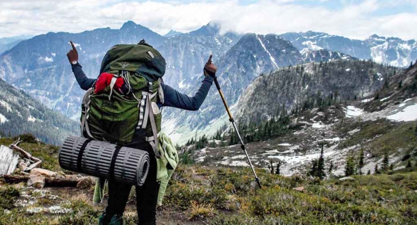 teen with raised hands looks out over mountain vista on backpacking expedition with outward bound